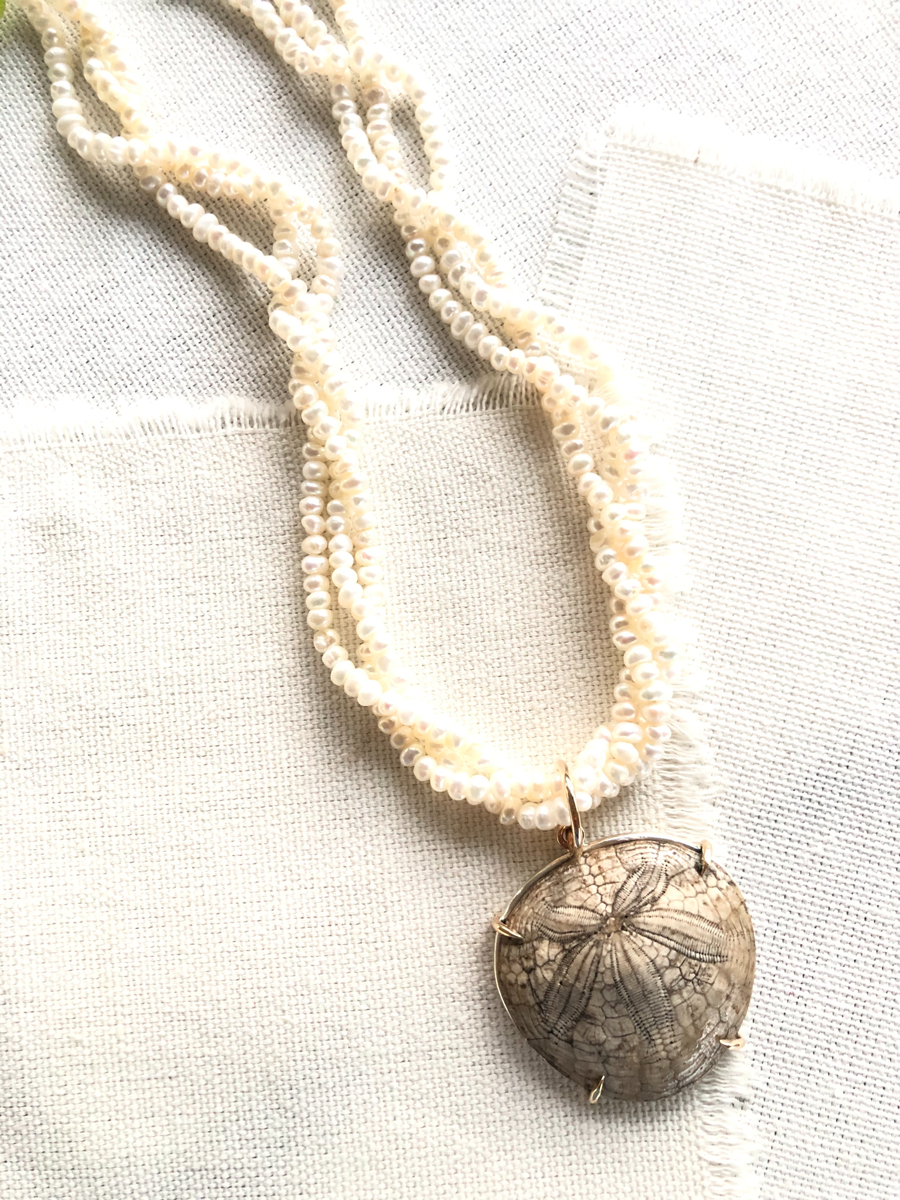 This is a one of a kind artisan made fossilized sand dollar on seed pearls necklace.