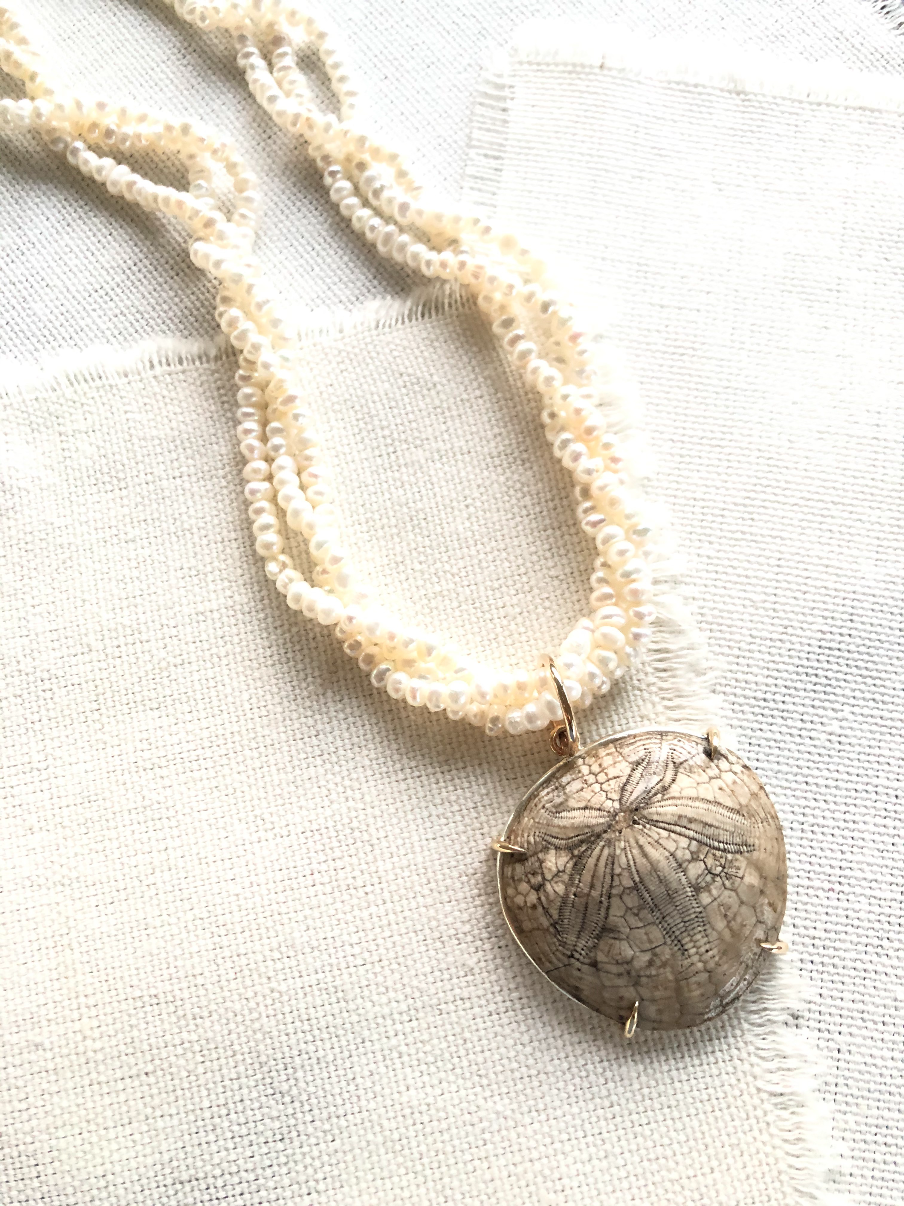 This is a one of a kind artisan made fossilized sand dollar on seed pearls necklace.
